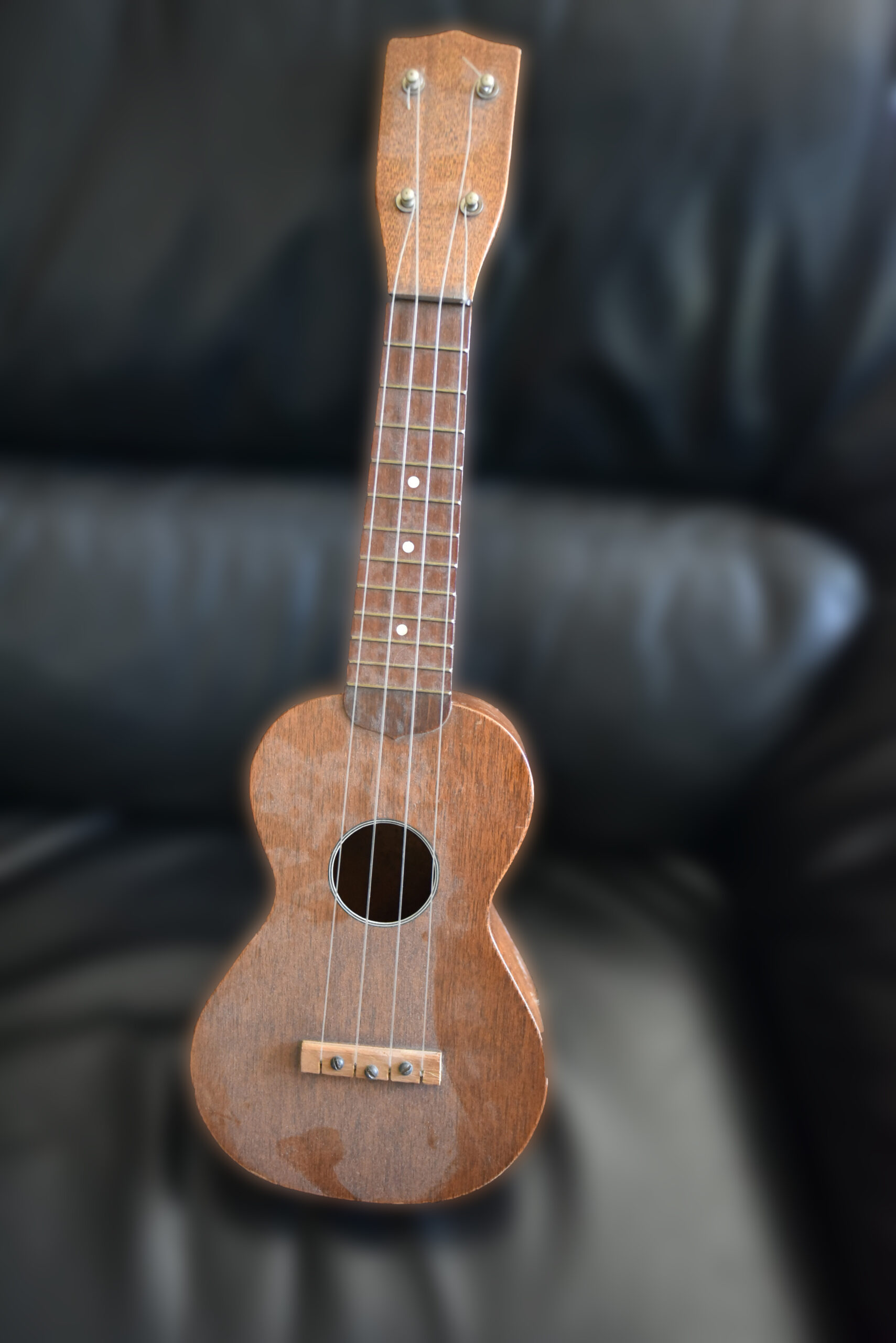 A small dusty ukulele sitting on a couch